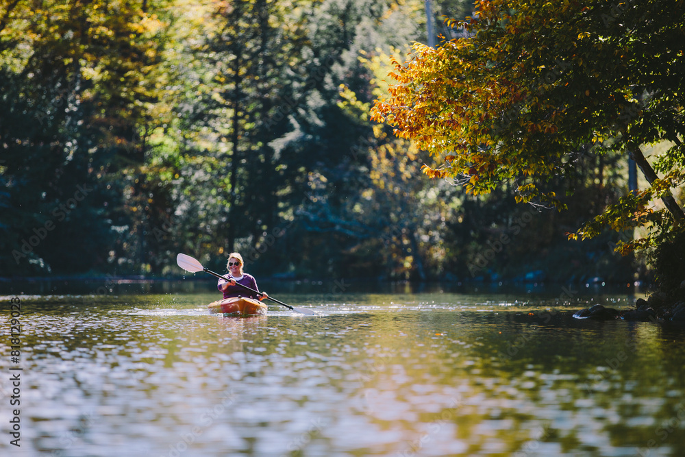 Woman kayaking on a lake during peak autumn foliage smiling with blonde hair and paddle. Woman kayaking on a lake during peak autumn foliage smiling with blonde hair and paddle.