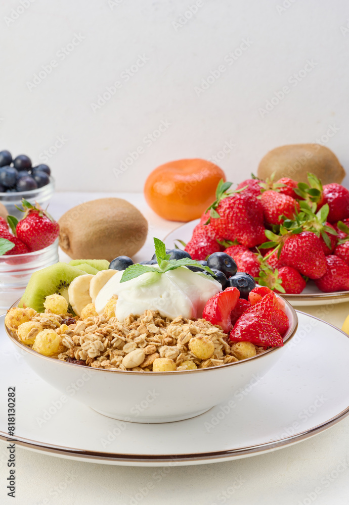 Granola with strawberries, kiwi, banana and blueberries in a round plate topped with yogurt on the table. Granola with strawberries, kiwi, banana and blueberries in a round plate topped with yogurt on the table.