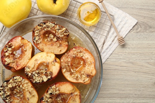 Delicious baked quinces with nuts in bowl, honey and fresh fruits on wooden table, flat lay. Space for text