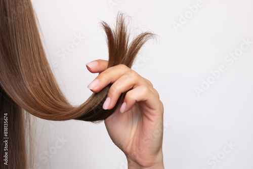 A woman holds in her hand a strand of hair with damaged, dry, split ends, close-up. Isolated on a white background. Hair care concept. Beauty and health. Treatment. Hairdressing services. A haircut