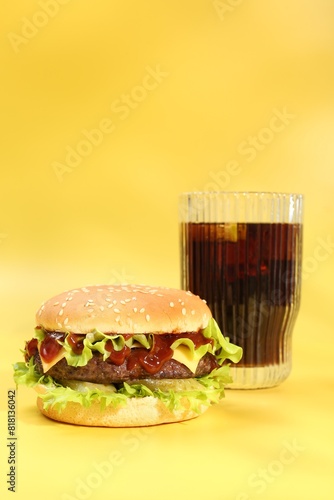 Burger with delicious patty and soda drink on yellow background