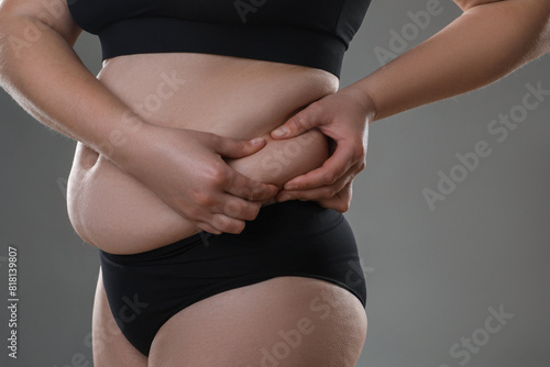 Woman touching belly fat on grey background, closeup. Overweight problem photo