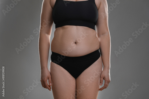 Woman with excessive belly fat on grey background, closeup. Overweight problem © New Africa