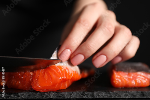 Chef removing scales from salmon for sushi at dark table, closeup