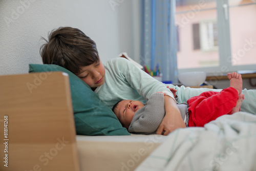 Older sibling lying down with newborn baby, both resting peacefully. The room’s soft lighting and cozy atmosphere emphasize the loving and serene sibling bond