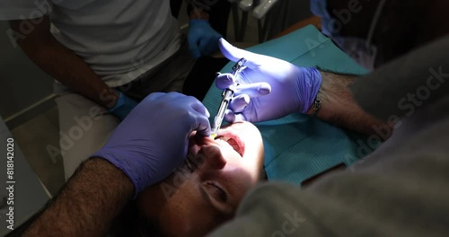 Dentist does anesthetic prick with syringe in mouth of patient illuminating with light. Doctor prepares woman for procedure in dental clinic photo