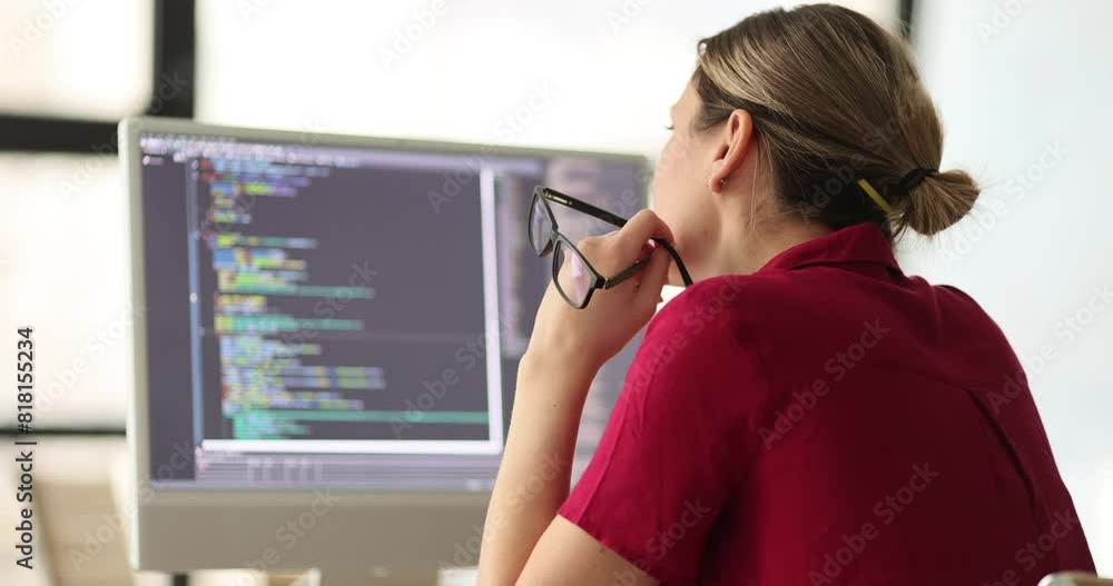 Woman programmer inspects code looking for errors sitting at workplace in office. Female employee with glasses in hand looks at monitor screen with program slow motion