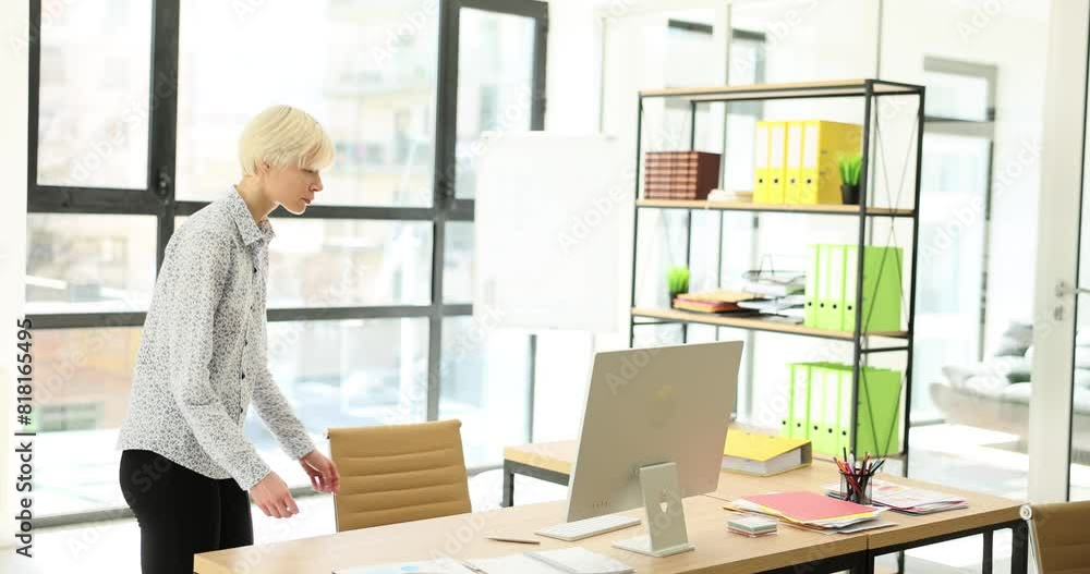Blonde manager goes across sunny spacious premise to wooden desk with computer. Female in classic shirt stops and leans on table to look at monitor screen slow motion Blonde manager goes across sunny spacious premise to wooden desk with computer. Female in classic shirt stops and leans on table to look at monitor screen slow motion