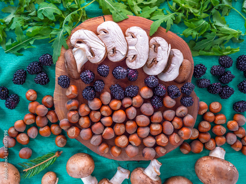 Obraz na płótnie Healthy autumn food selection: white sliced mushrooms, shelled hazelnuts, arugula rocket salad, fresh blackberries and tiny fir branch on green background. w salonie