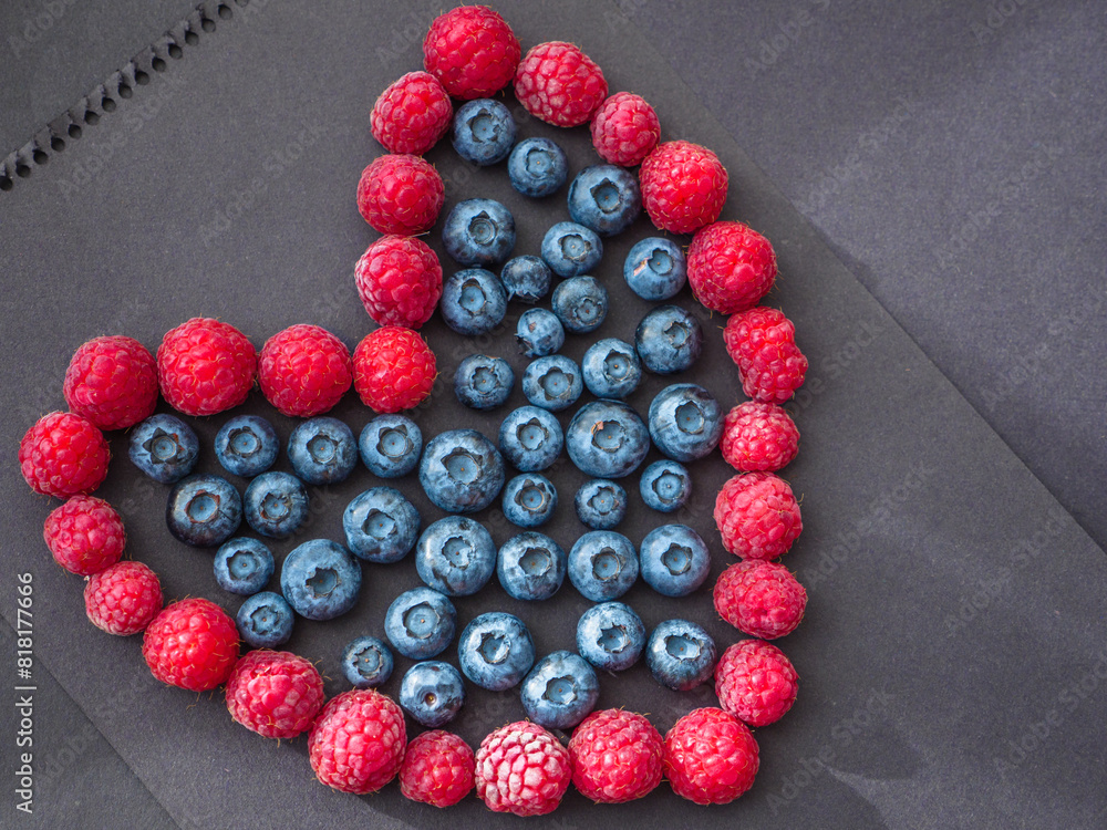 Heart shape love sign made by fresh raspberries and blueberries on black paper. Love and Valentine's day concept.