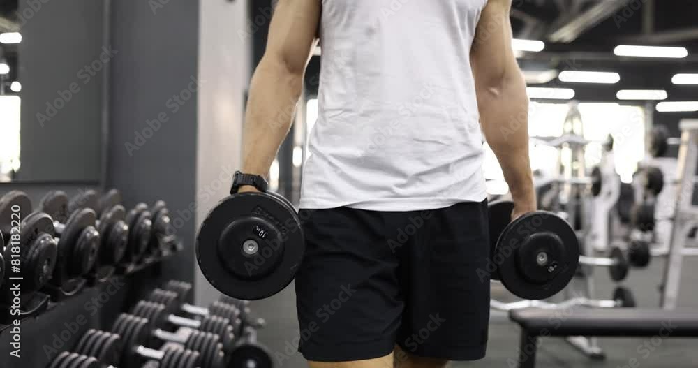 Strong man walks across gym holding heavy dumbbells in hands. Fit athlete in sportswear prepares for intensive training with weight slow motion Strong man walks across gym holding heavy dumbbells in hands. Fit athlete in sportswear prepares for intensive training with weight slow motion