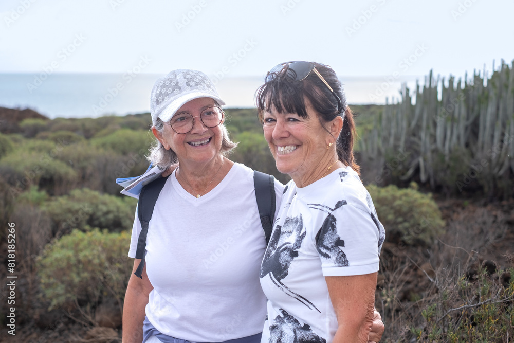 Cheerful couple of senior female friends enjoying healthy lifestyle walking outdoor along the sea in Tenerife island, horizon over sea on background