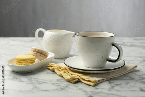 Tasty cappuccino in cup, macarons, pitcher and saucer on white marble table