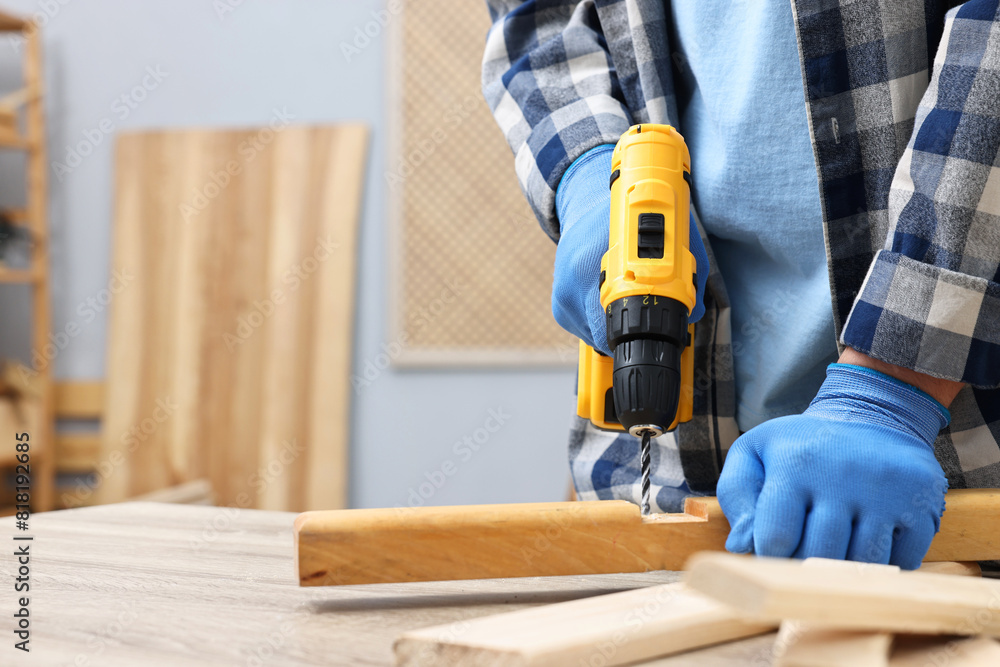 Young handyman working with electric drill at table in workshop, closeup Young handyman working with electric drill at table in workshop, closeup