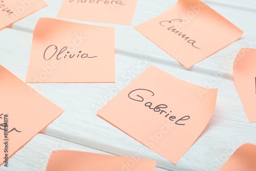 Paper stickers with different names on white wooden table, closeup. Choosing baby's name