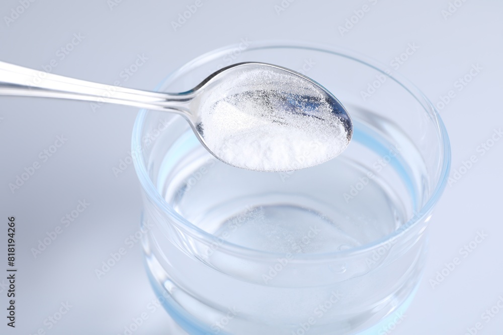 Adding baking soda into glass of water on light background, closeup