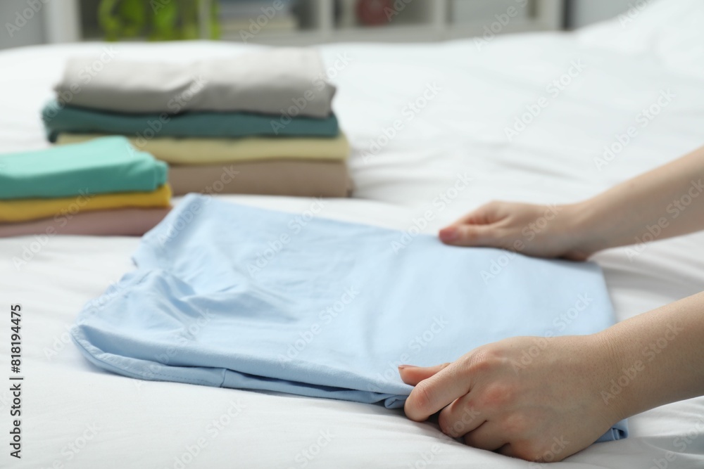 Woman folding clothes on bed indoors, closeup Woman folding clothes on bed indoors, closeup
