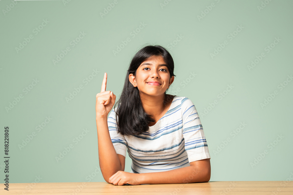 Happy Indian asian teenage girl showing or pointing something sitting at table Happy Indian asian teenage girl showing or pointing something sitting at table