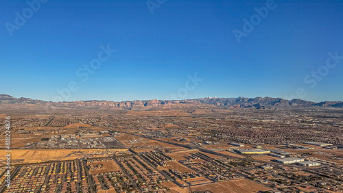 Las Vegas, NV, USA - May 11, 2024: Flying over brown wide desert landscape under blue morning sky SW from city. One-story house neighborhoods. Mountain range on horizon, 1 snow peak