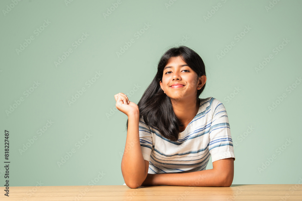 Indian asian small girl sitting at table against plain green background Indian asian small girl sitting at table against plain green background