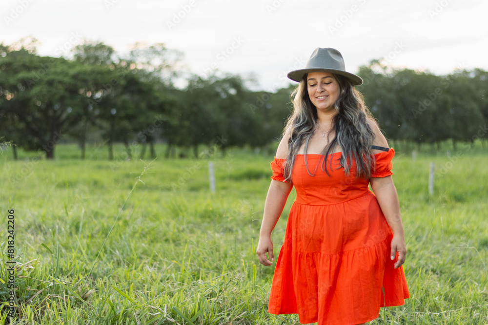 Obraz premium young latin woman walking free and alone in a grassy field, smiling and looking at the ground.