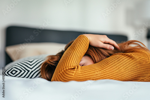 Woman in yellow sweater lying on a bed burying head between her arms, exhausted, tiredness, embarrassing, disappointed,