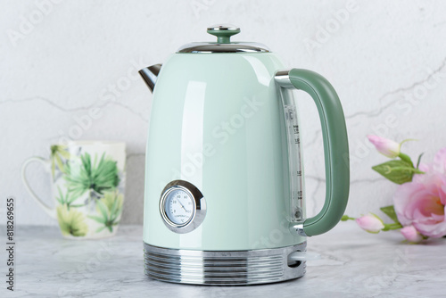 Modern electric kettle on kitchen table with cup and roses in background.