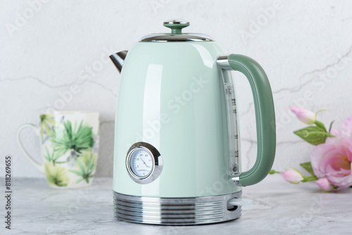 Modern electric kettle on kitchen table with cup and roses in background. © svdolgov