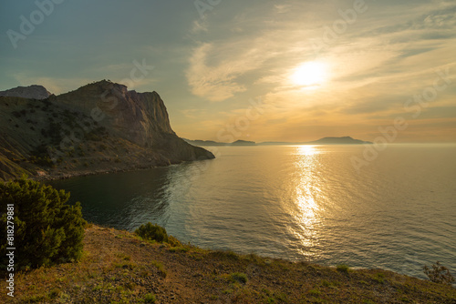 A beautiful sunset over the ocean with a mountain in the background. The sky is filled with clouds and the sun is setting. The water is calm and the sky is a mix of orange and pink hues. © svetograph