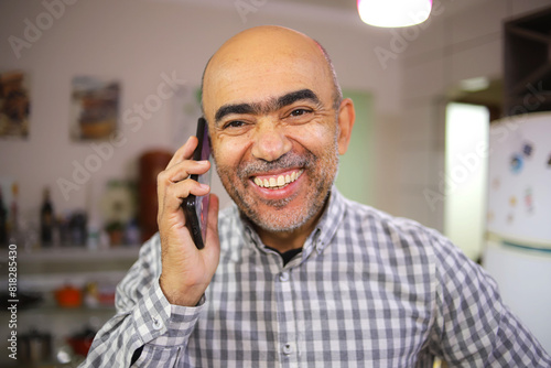 Homem de 50 anos, com barba branca , sorrindo, alegre em um ambiente interno em close, falando ao telefone
