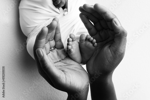 The palms of the father, the mother are holding the foot of the newborn baby. Feet of the newborn on the palms of the parents. Studio macro black and white photo of a child's toes, heels and feet.
