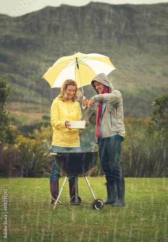 Cheerful  couple and rain at barbecue in outdoor on vacation or picnic as family in together. Happy woman  man and smile with umbrella  grill or bbq for celebration  birthday or event in Scotland