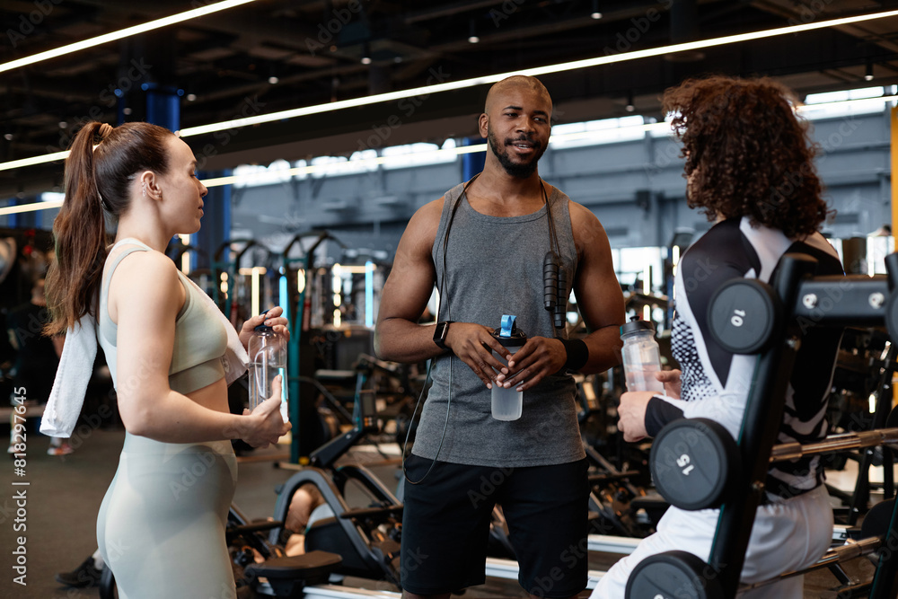 Fototapeta premium Waist up portrait of muscular African American man as fitness coach talking to two clients in gym giving instructions before training