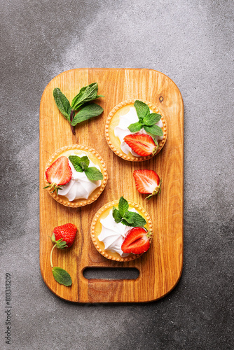 Fresh homemade tart with cream, strawberries and mint leaves on dark stone background with copy space for your design top view. Vertical image.