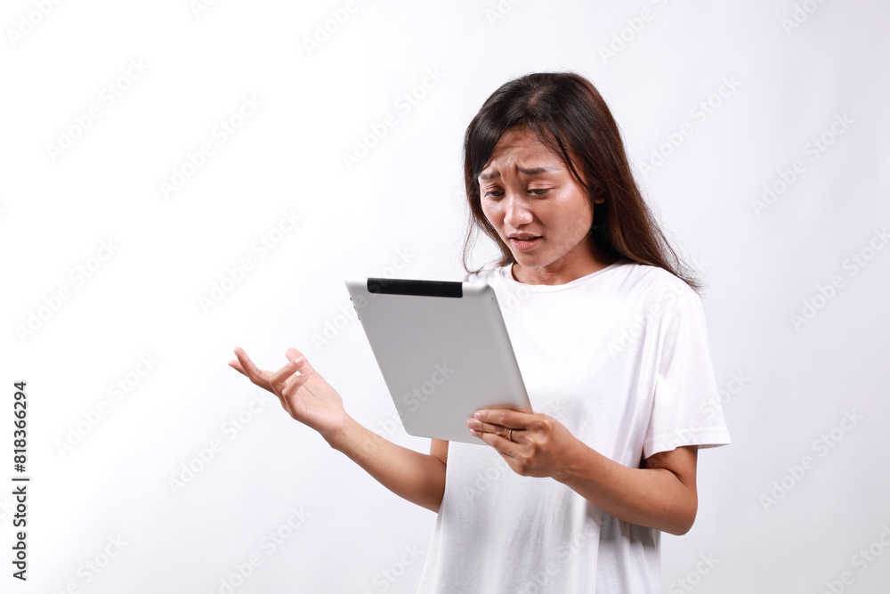 Attractive woman holding a digital tablet while standing over white background with confused face expression Attractive woman holding a digital tablet while standing over white background with confused face expression