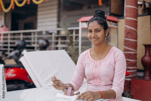 Happy young woman in pink dress with dark skin enjoys sweet dessert, sits at table outside in .