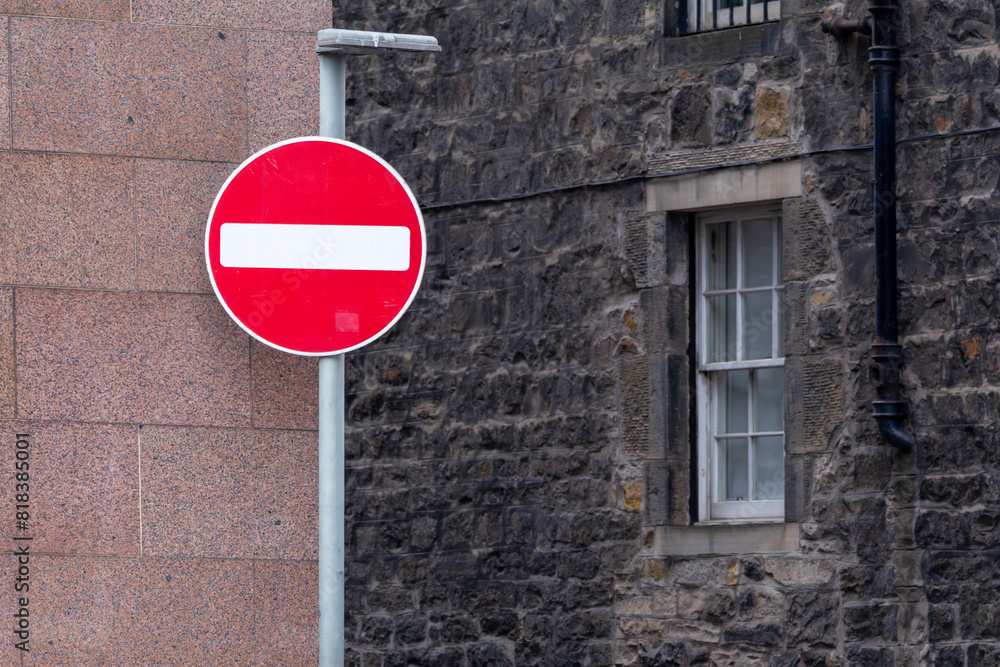 A circular red sign with a white bar indicating NO ENTRY on a grey metal post against buildings. Pay attention. A circular red sign with a white bar indicating NO ENTRY on a grey metal post against buildings. Pay attention.
