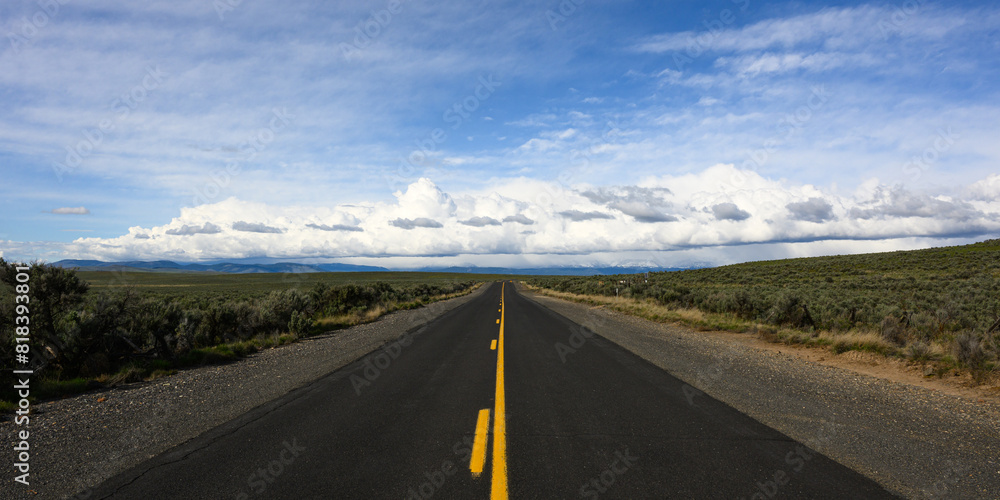 Open road of balck asphalt with yellow line in Eastern Oregon leading to big sky with white clouds on horizon Open road of balck asphalt with yellow line in Eastern Oregon leading to big sky with white clouds on horizon
