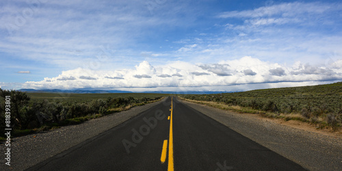 Open road of balck asphalt with yellow line in Eastern Oregon leading to big sky with white clouds on horizon