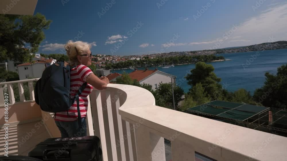 A mature woman stands on a balcony overlooking the sea. Suitcases in the foreground. Tourism concept. Croatia. A mature woman stands on a balcony overlooking the sea. Suitcases in the foreground. Tourism concept. Croatia.