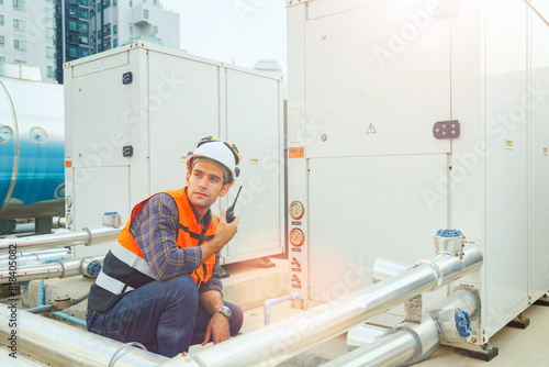 HAVC refrigeration system mechanic daily inspection refrigeration equipment on the roof building checking pressure and electrical control systems using radio communications to report technician team. photo