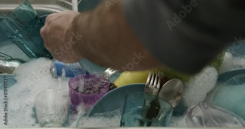 A man is washing dishes in a kitchen sink, scrubbing utensils and plates with soap and running water. photo