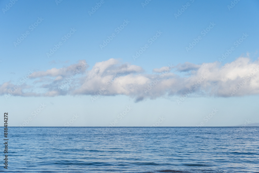 Obraz premium Peaceful, serene, and calming blue nature background of flat Pacific Ocean reaching to a blue sky horizon with line of white fluffy clouds, as a nature background 