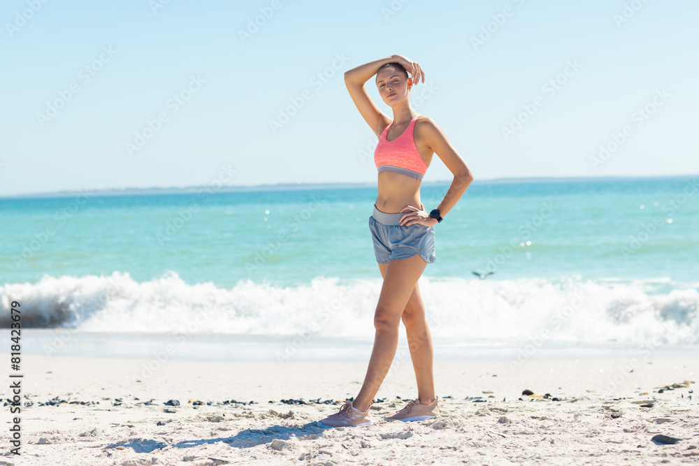 At beach, Caucasian young woman standing, hand on head, looking away At beach, Caucasian young woman standing, hand on head, looking away