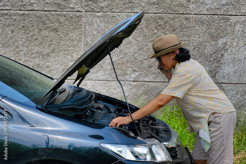 Woman fixing her stalled car with opened bonnet, trying to call for help photo