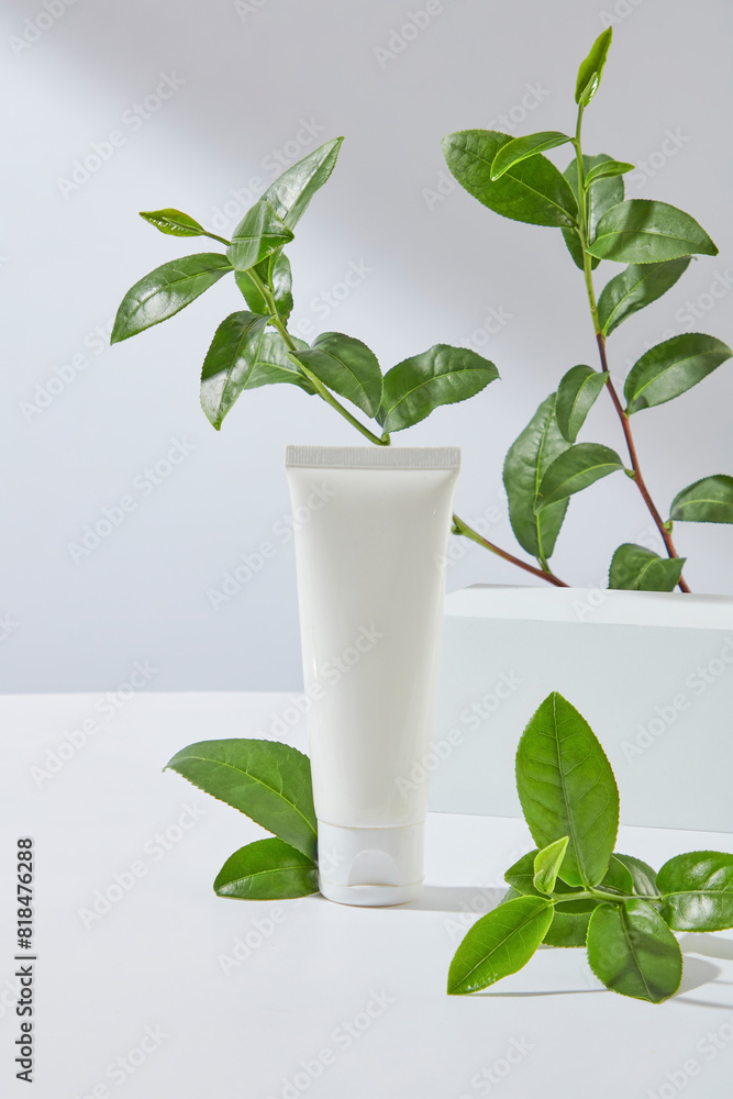 Minimalist advertising photo on white background with green color of tea leaves decoration, a cosmetic tube without label placed in center with a blank podium in back. Front view photo, copy space Minimalist advertising photo on white background with green color of tea leaves decoration, a cosmetic tube without label placed in center with a blank podium in back. Front view photo, copy space