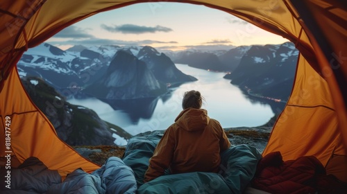 Person gazing at a serene fjord view, surrounded by mountains, from the cozy interior of an open tent at dawn.