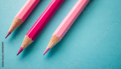 Three pink pencils aligned diagonally on a light blue background. The composition emphasizes simplicity and contrast, symbolizing creativity, education, and artistic inspiration