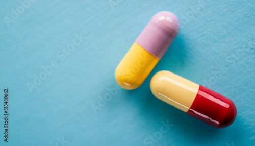 Two colorful medicine pill capsules lie on a light blue background. This top view, flat lay composition offers ample copy space, symbolizing health, medication, and pharmaceutical care