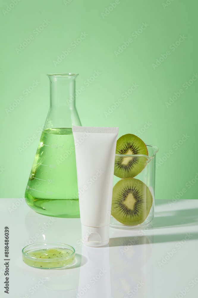 Over the green background, an unbranded tube in white color is displayed with a conical flask of liquid, a beaker of kiwi slices and a petri dish. Mockup of skin care cosmetic tube of beauty facial Over the green background, an unbranded tube in white color is displayed with a conical flask of liquid, a beaker of kiwi slices and a petri dish. Mockup of skin care cosmetic tube of beauty facial